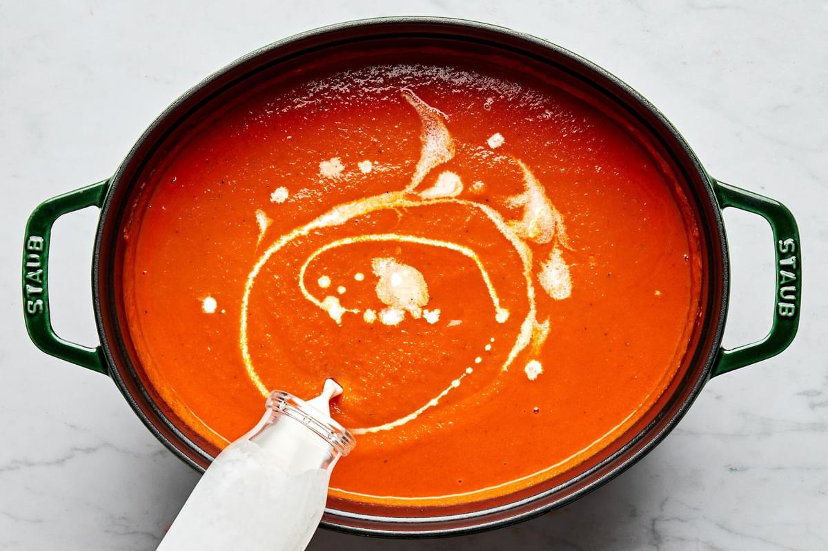 blended homemade tomato bisque in a pot with cream being poured in