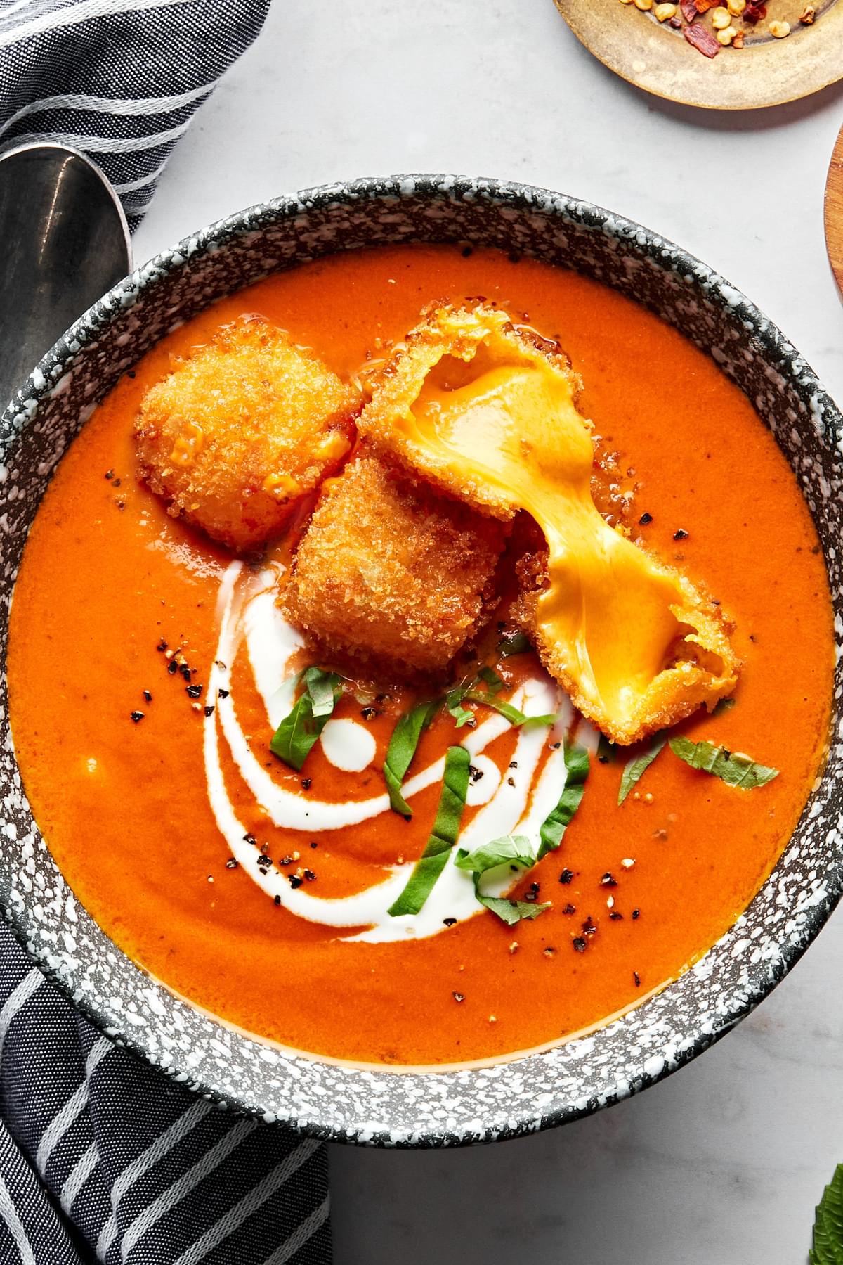 a bowl of homemade tomato bisque garnished with cream and fresh basil and topped with fried cheese