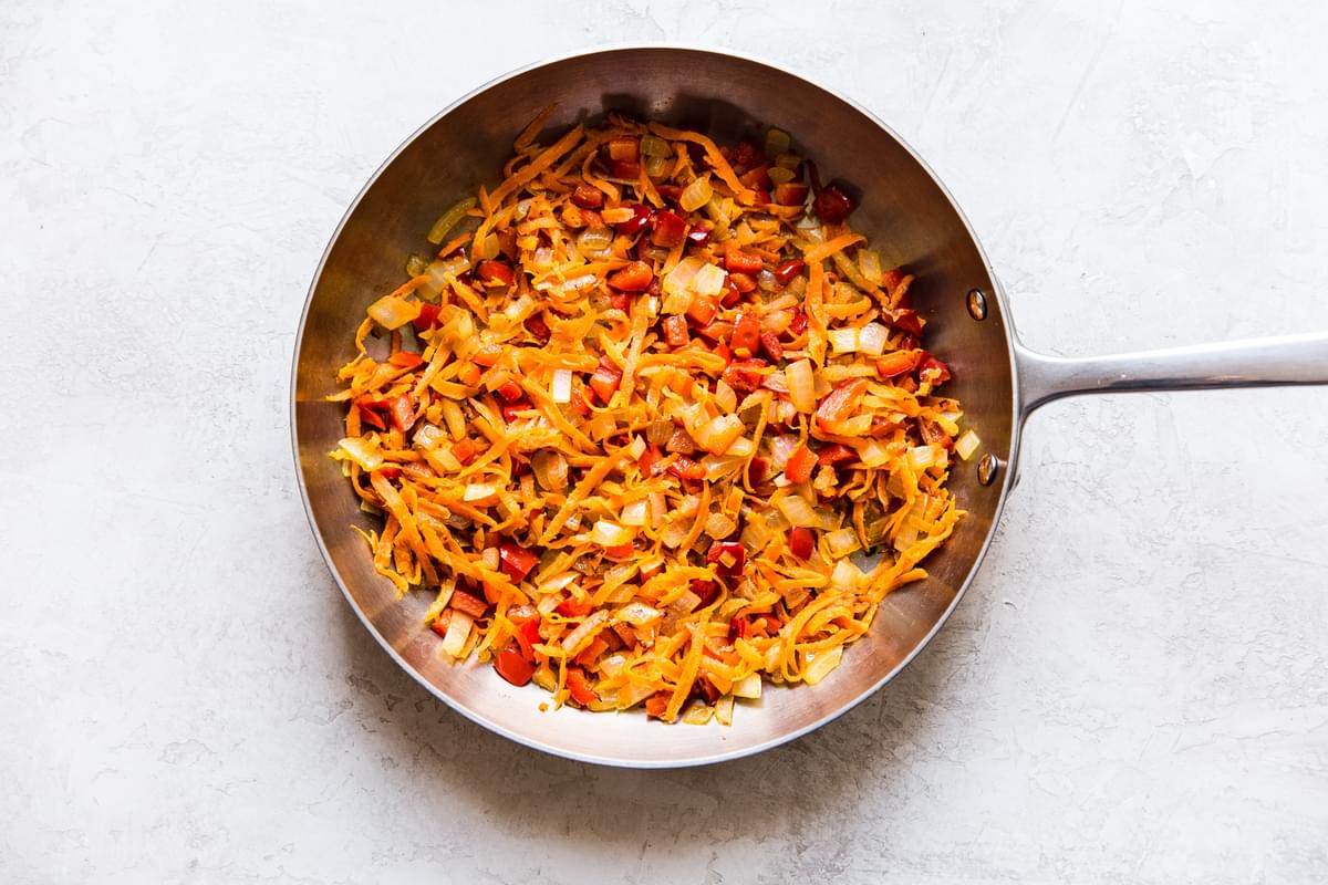 onions, bell peppers and shredded carrots sautéed in a pan.