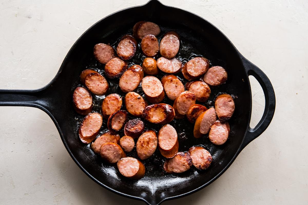 sliced sausage being browned in a cast iron skillet