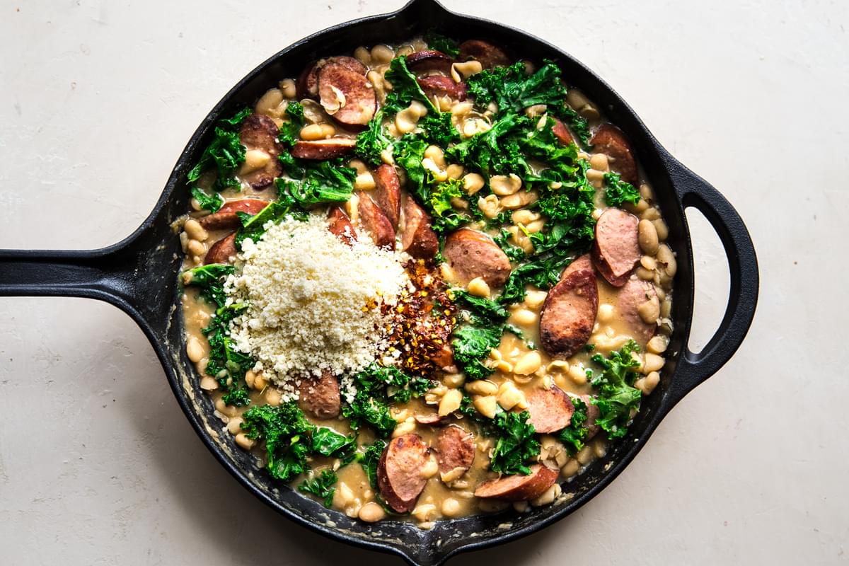 White Bean and sausage skillet dinner with garlic, chicken stock, kale and parmesan cheese being in a cast iron pan