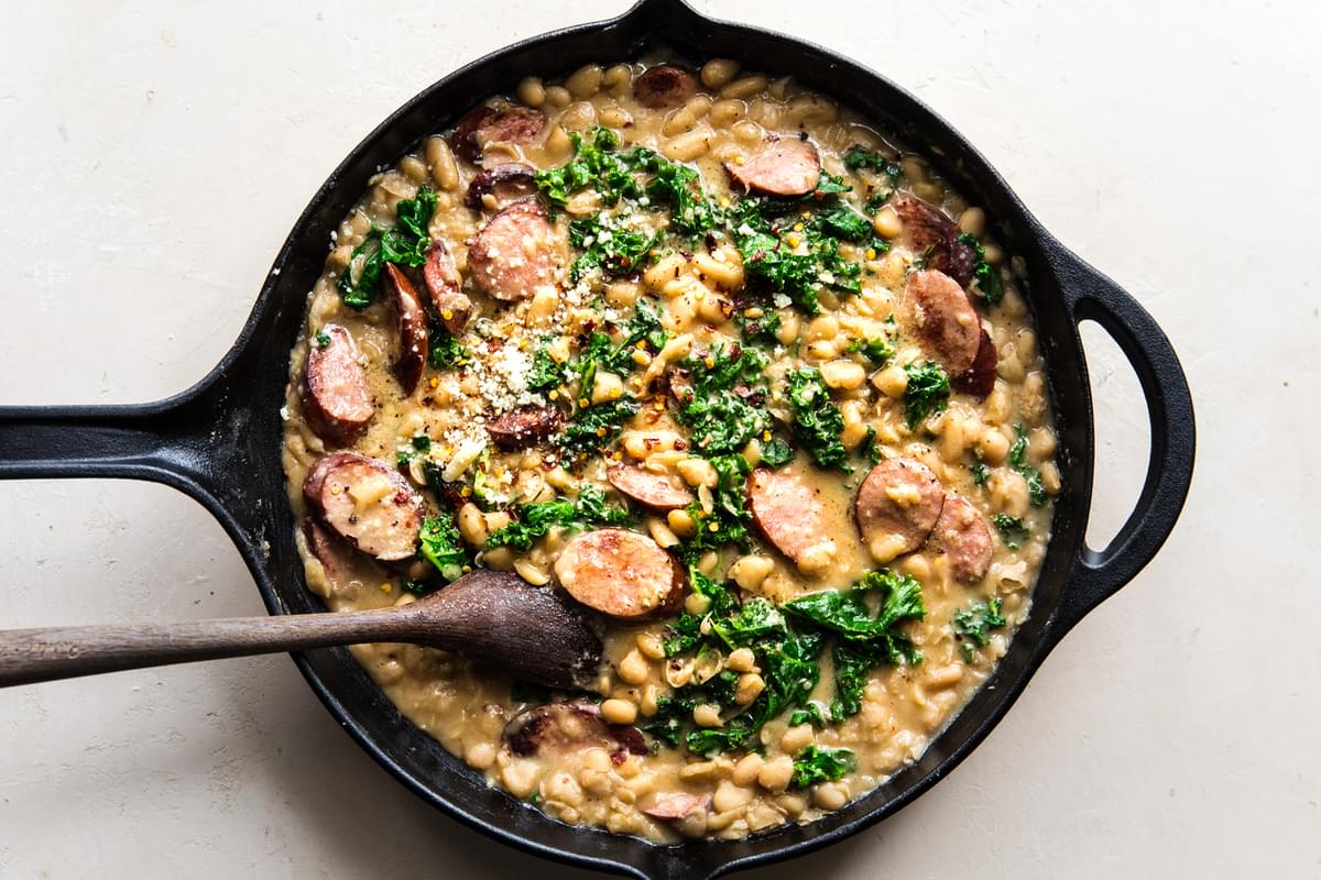 white bean and sausage skillet dinner with kale being stirred with a spoon