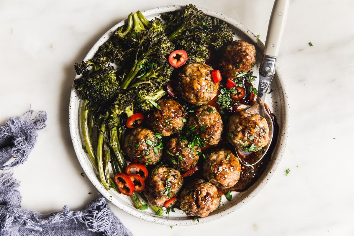 homemade baked teriyaki meatballs being served with roasted broccoli on a plate and drizzled with homemade teriyaki sauce