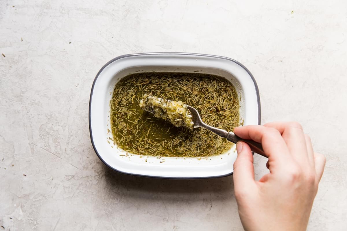 hand whisking dried herbs, melted butter and garlic in a small dish with a fork