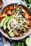 chicken tortilla soup with topped with sour cream avocado and tortilla strips and lime in a bowl