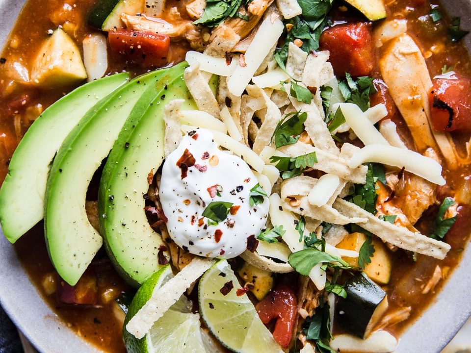 chicken tortilla soup with sour cream avocado and tortilla strips and lime