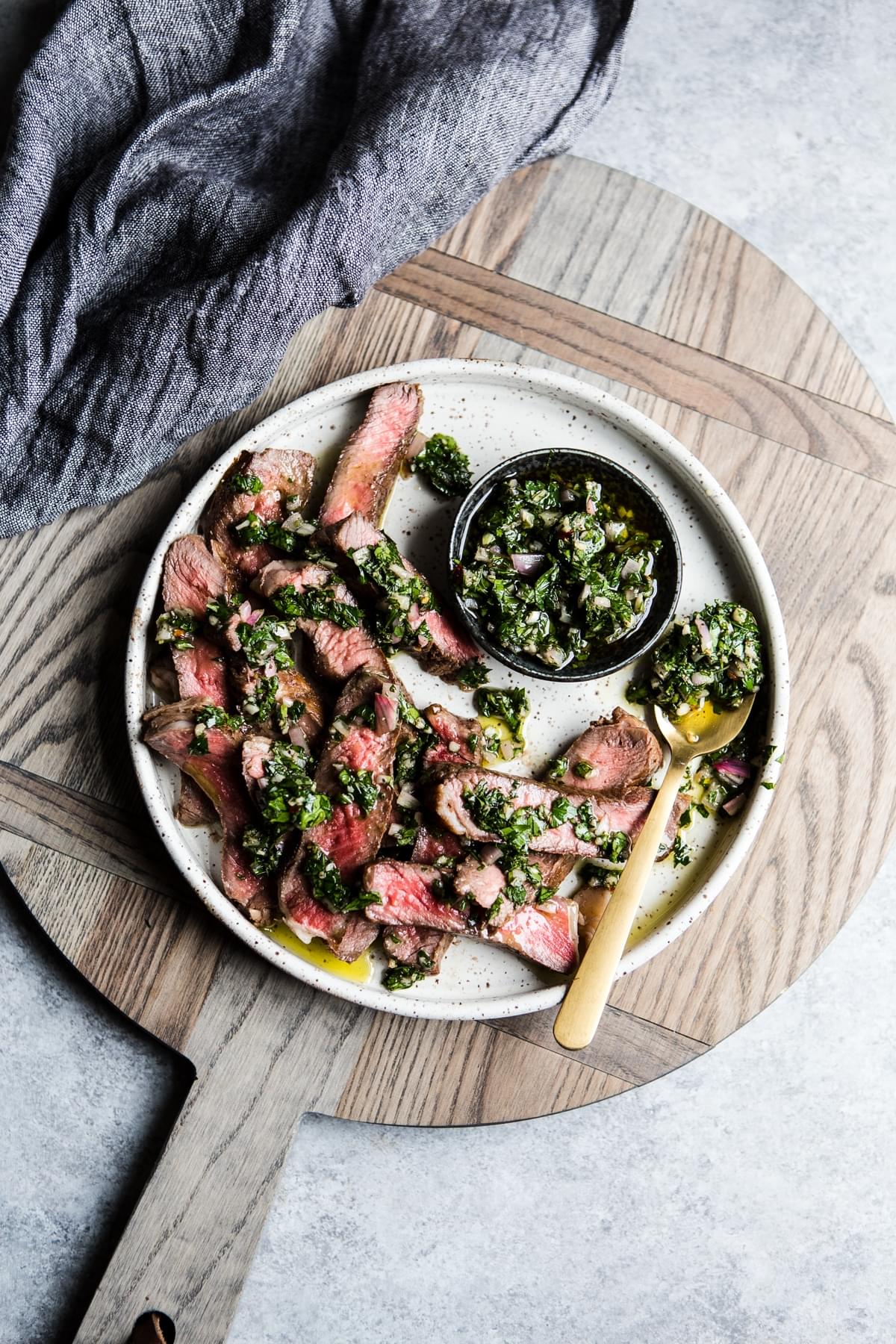 A plate of flank steak cooked medium drizzled with chimichurri sauce