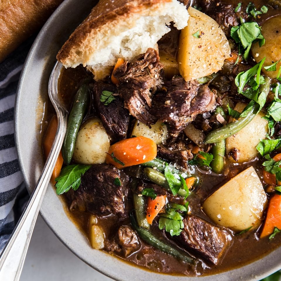 traditional beef stew in a bowl with a spoon with carrots and potatoes and green beans