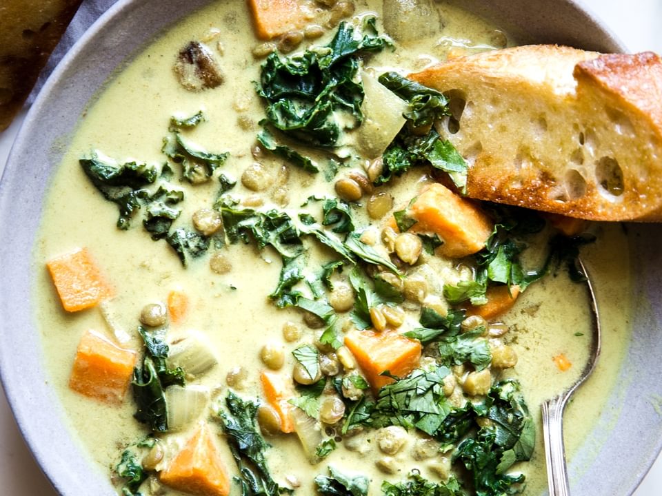 coconut curry lentil soup with kale and sweet potatoes in a bowl with a spoon