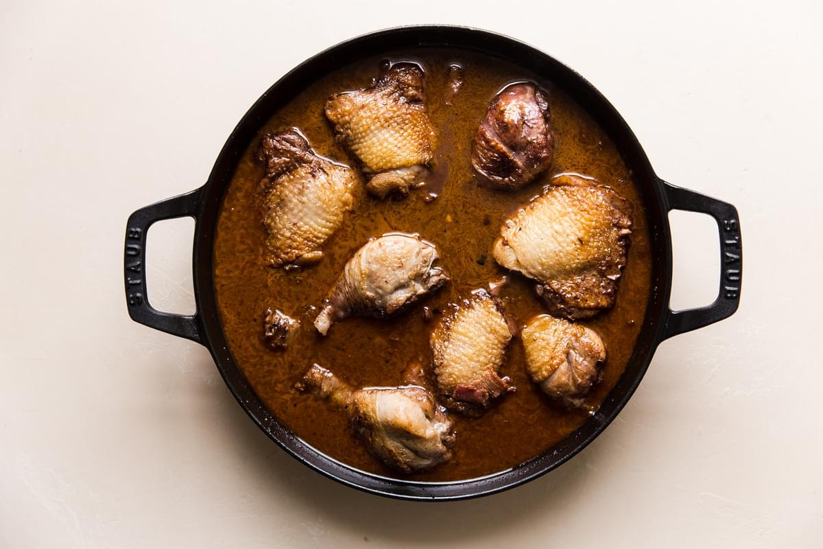 browned chicken thighs simmering in stock and wine in a braising dish