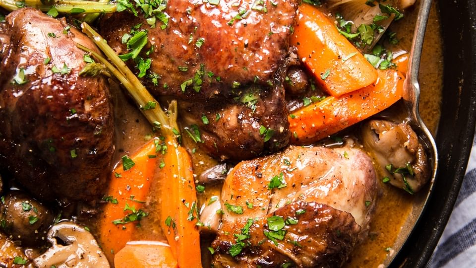 Coq Au Vin with carrots, mushrooms and chicken in a pot with a spoon
