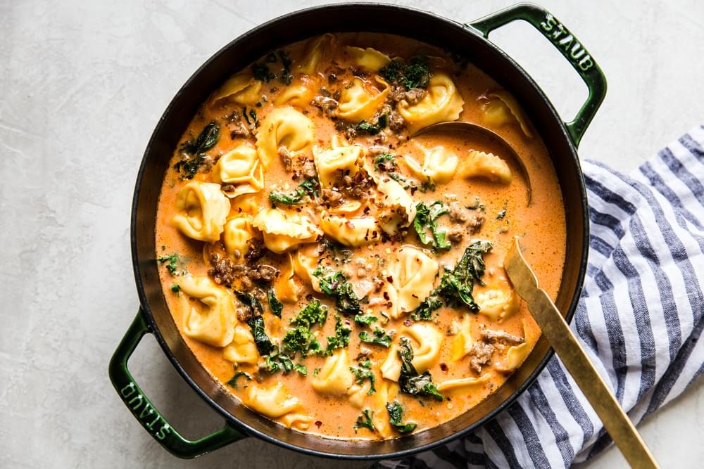 homemade creamy tomato tortellini soup with sausage and kale in a large soup pot with a ladle