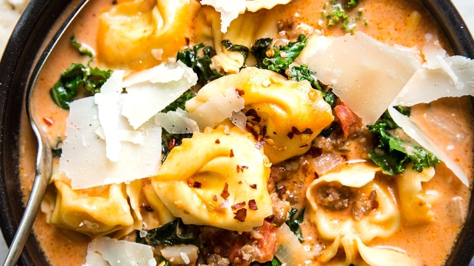 ceramic bowl of creamy tortellini soup with sausage and kale topped with fresh parmesan