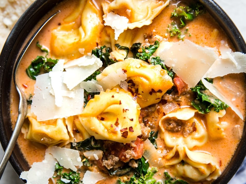 ceramic bowl of creamy tortellini soup with sausage and kale topped with fresh parmesan