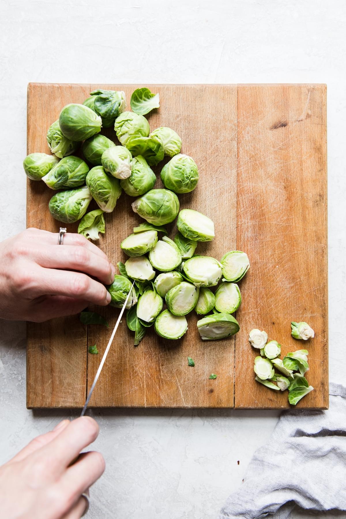hands slicing brussels sprouts on a cutting board with a knife