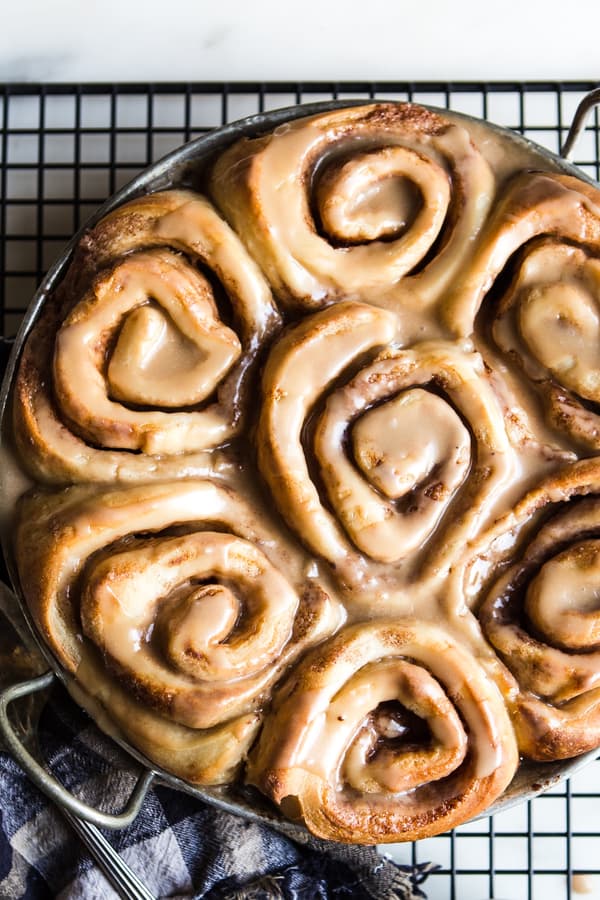 Dairy free cinnamon rolls in a pan on a baking sheet with maple frosting