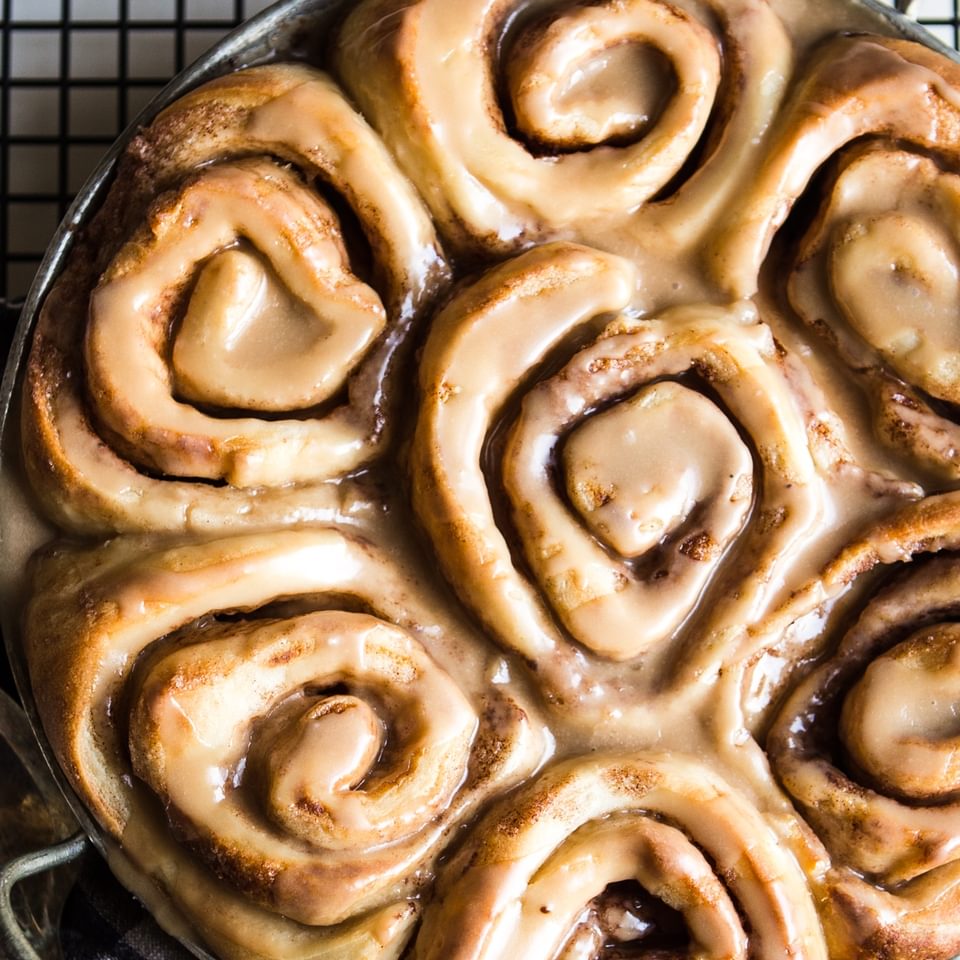 Dairy free cinnamon rolls in a pan on a baking sheet with maple frosting