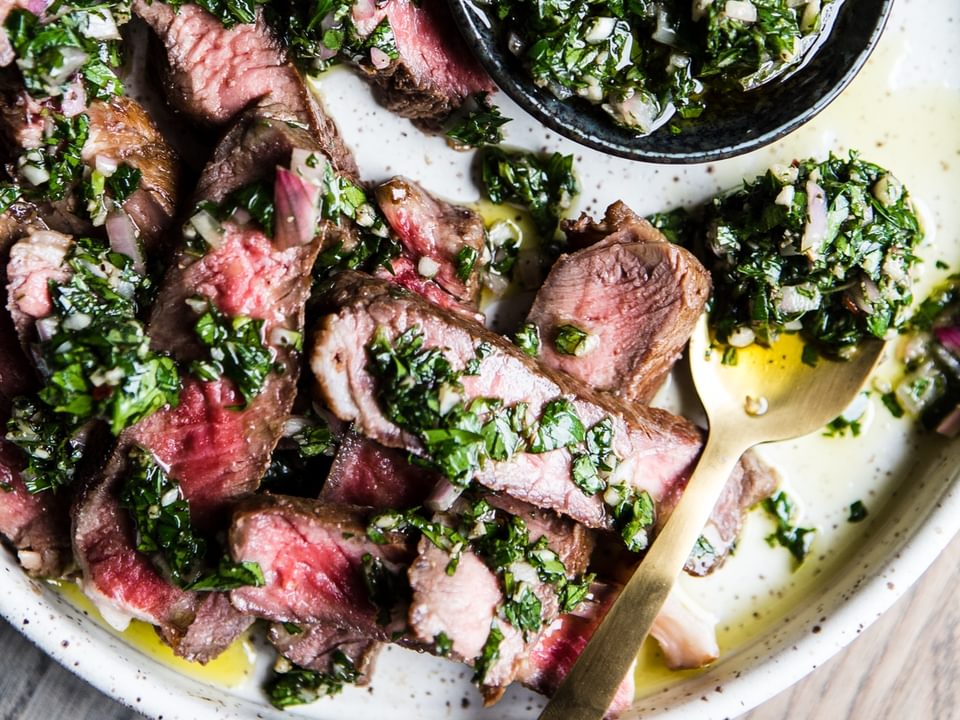 Flank steak sliced on a plate drizzled with chimichurri sauce