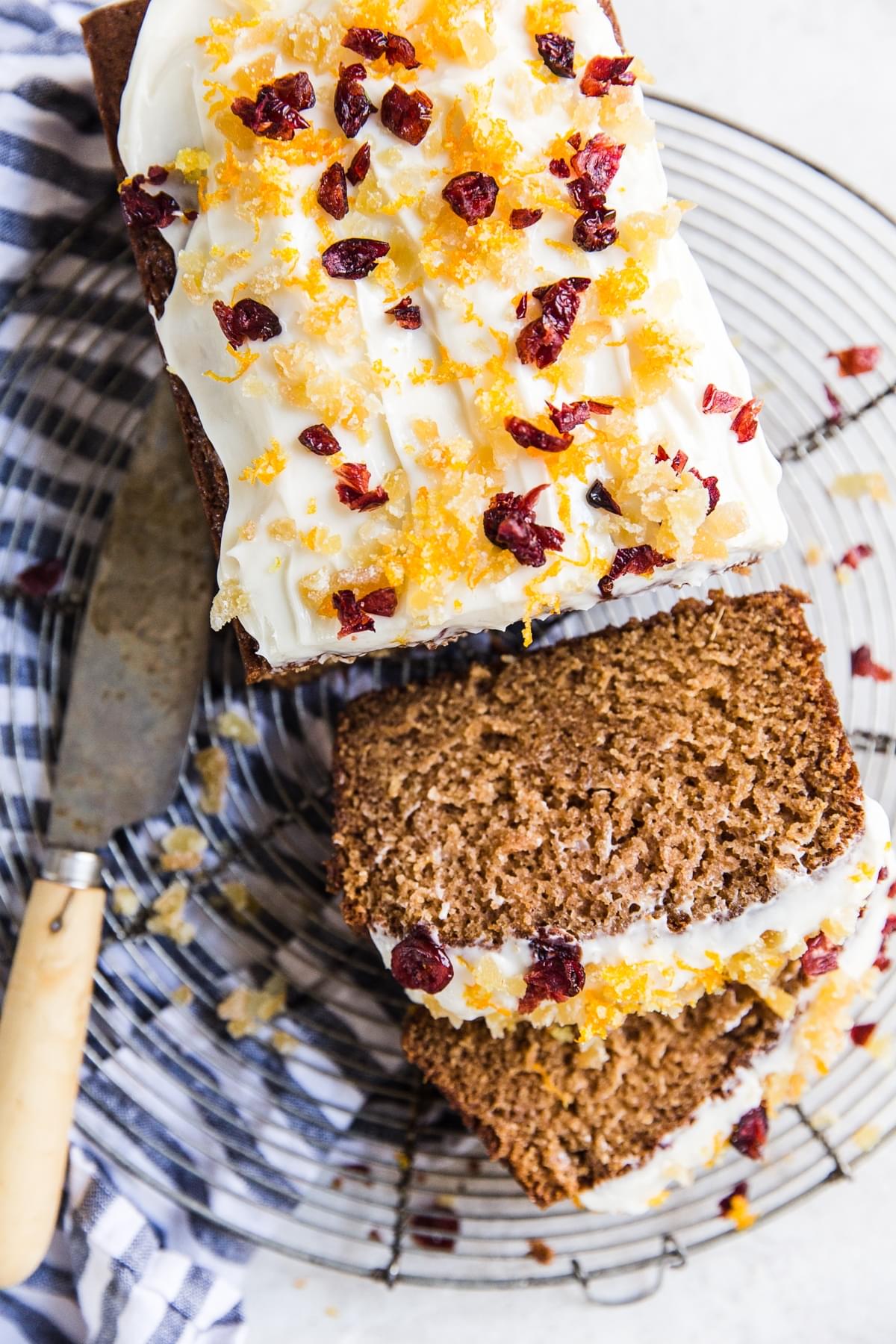 Sliced gingerbread loaf with cream cheese frosting with candied ginger, dried cranberries and orange zest.
