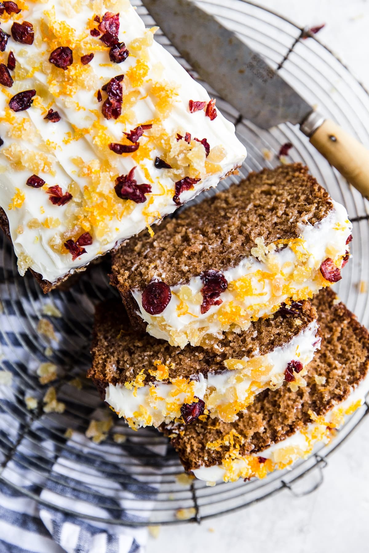 Gingerbread Loaf With Cream Cheese Icing orange zest, candied ginger and dried cranberries sliced on a cooling rack