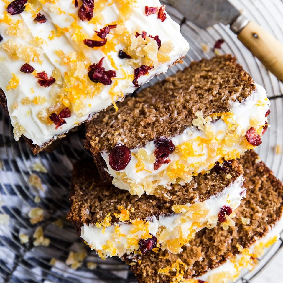 Gingerbread Loaf With Cream Cheese Icing orange zest, candied ginger and dried cranberries sliced on a cooling rack