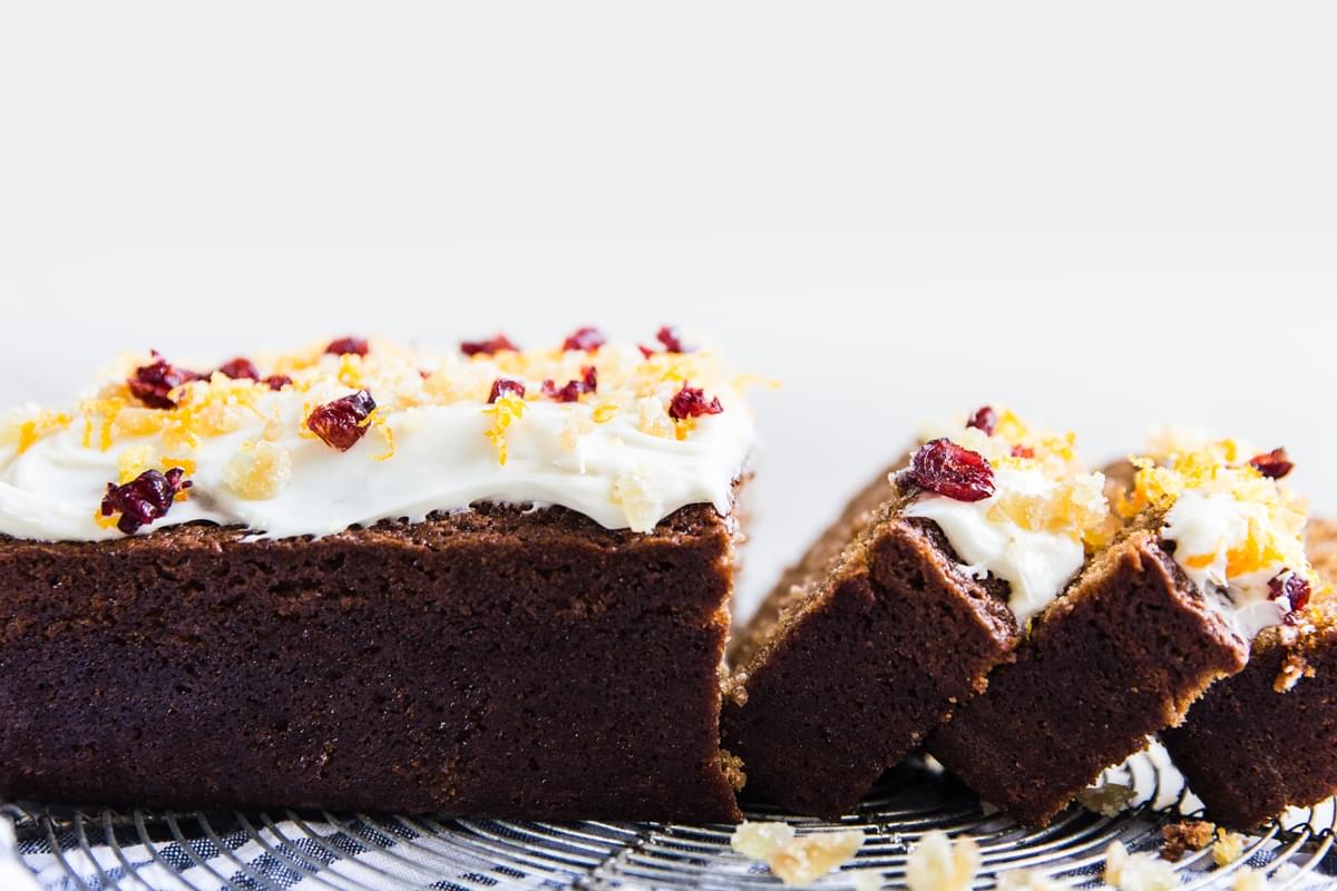 Sliced gingerbread loaf with cream cheese frosting with candied ginger, dried cranberries and orange zest.