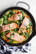 four salmon filets in a cast iron skillet w with lime, red bell peppers, cilantro and  green curry sauce