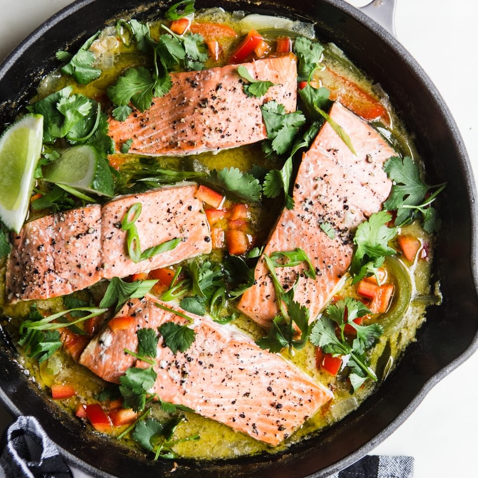 four salmon filets in a cast iron skillet w with lime, red bell peppers, cilantro and  green curry sauce