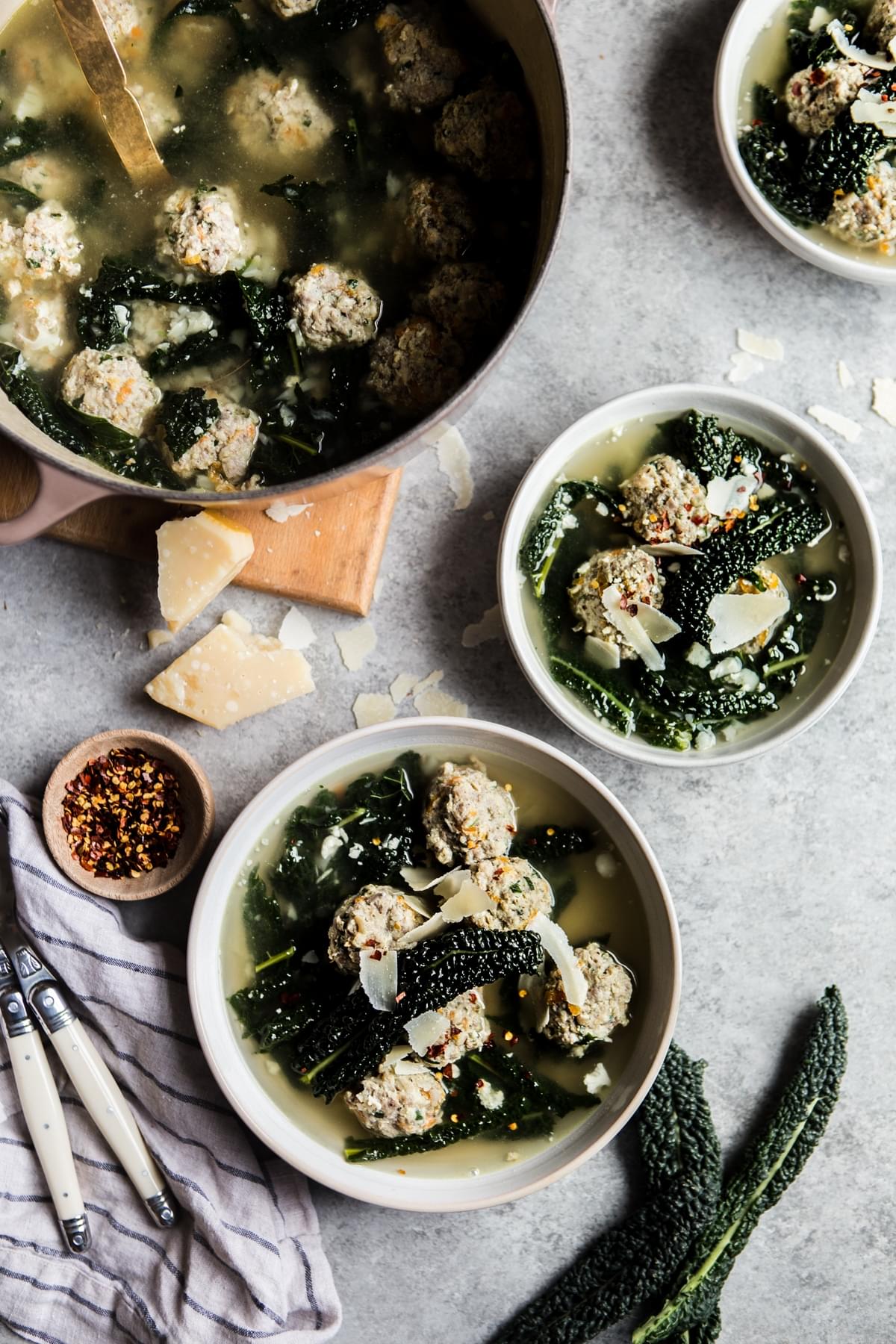 A pot of Italian Wedding Soup with red pepper flakes, parmesan, kale and chicken and pork meatballs