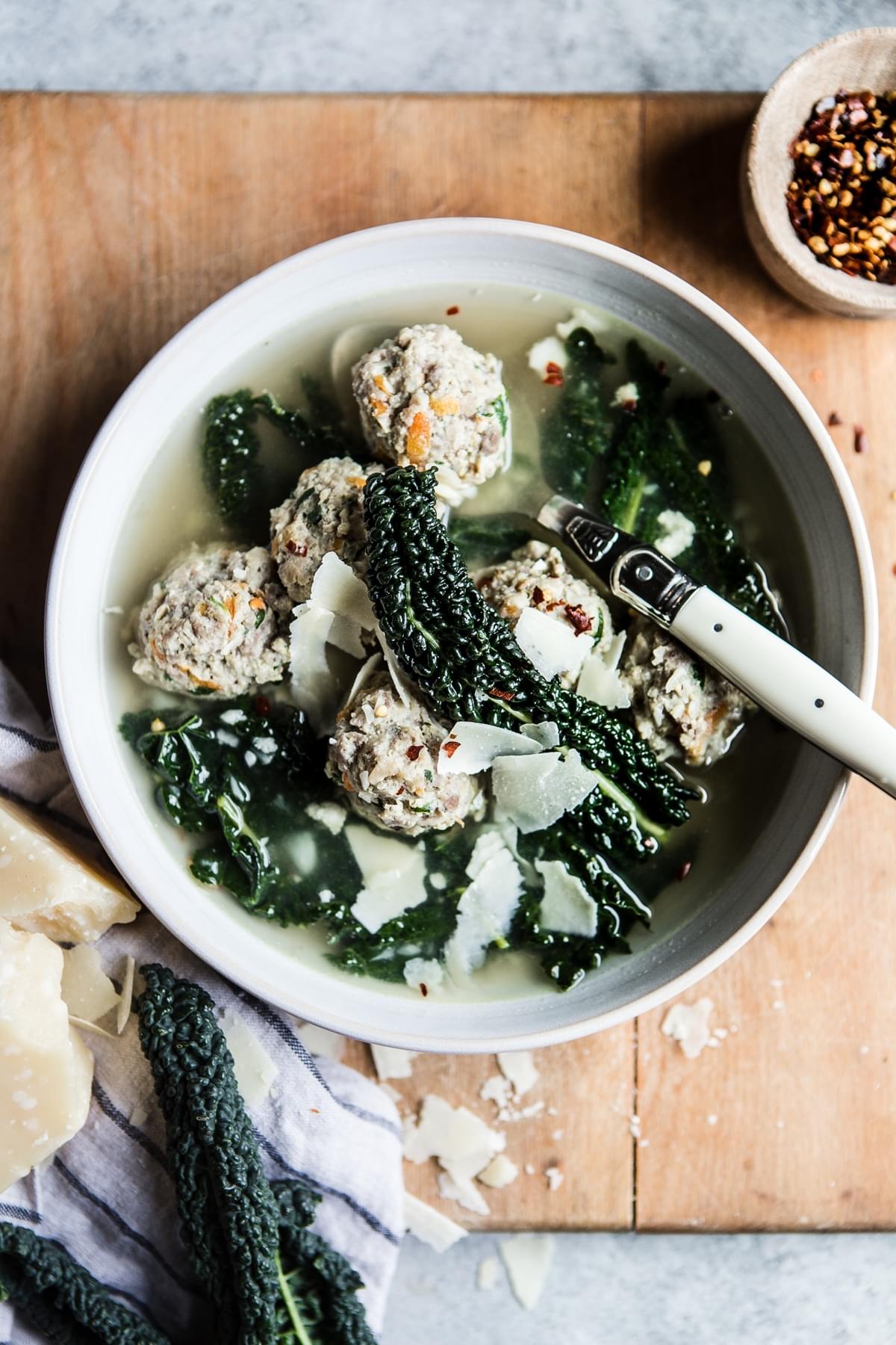 Homemade Italian Wedding Soup in a bowl with parmesan cheese, chicken meatballs with a spoon
