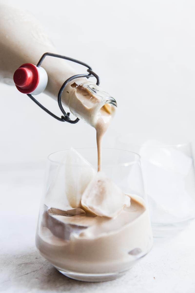 Homemade Irish Cream being poured from a bottle into a glass with ice.