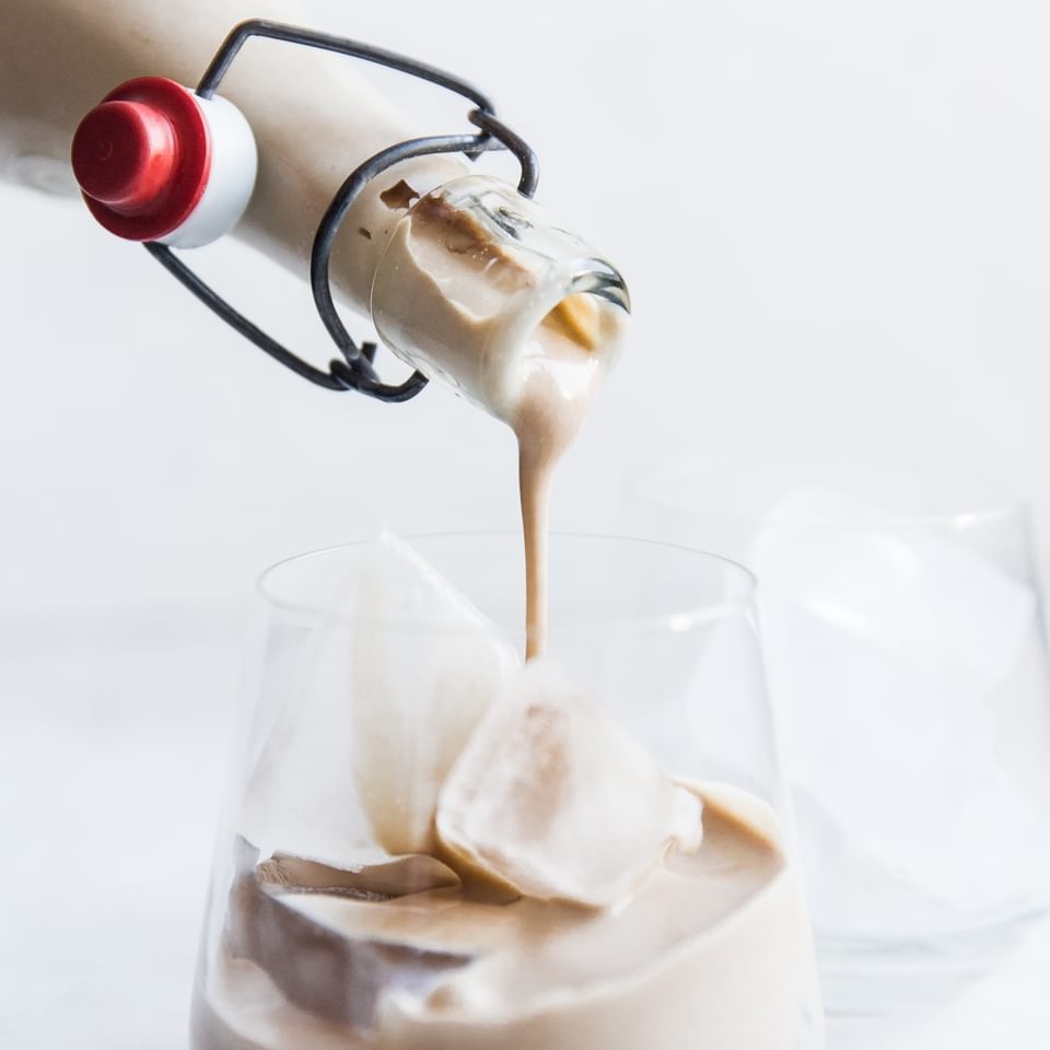 Homemade Irish Cream being poured from a bottle into a glass with ice.