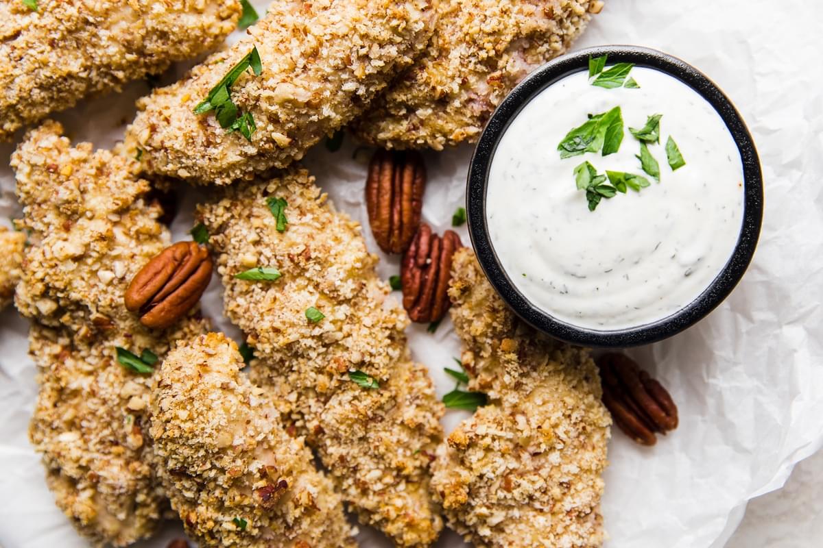 Pecan Crusted Chicken Tenders on parchment paper with a small bowl of buttermilk ranch next to them