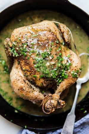 cast iron skillet with whole roasted chicken topped with butter and lemon pan sauce