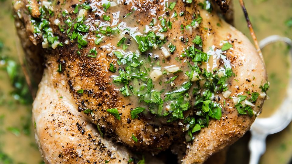 cast iron skillet with whole roasted chicken topped with butter and lemon pan sauce