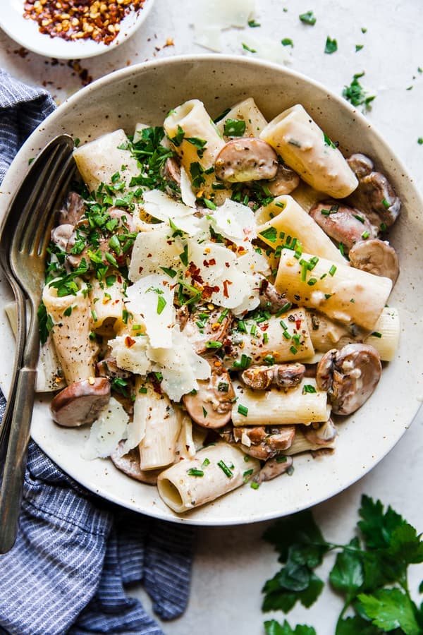 bowl of rigatoni with mushroom cream sauce topped with fresh parsley and shaved parmesan cheese with red pepper flakes