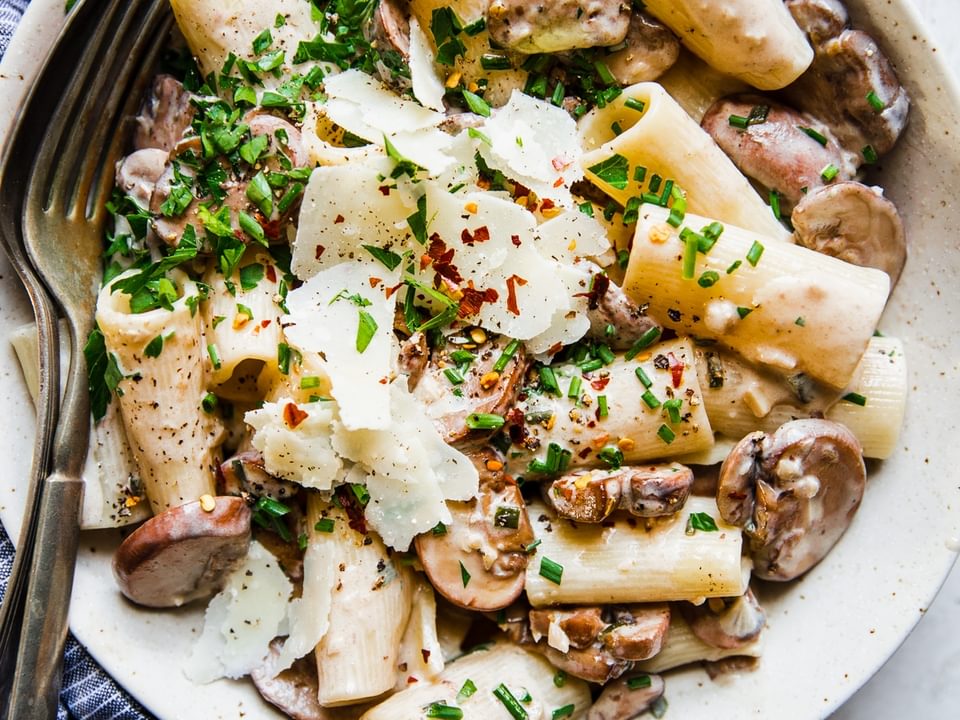 bowl of rigatoni with mushroom cream sauce topped with fresh parsley and shaved parmesan cheese with red pepper flakes