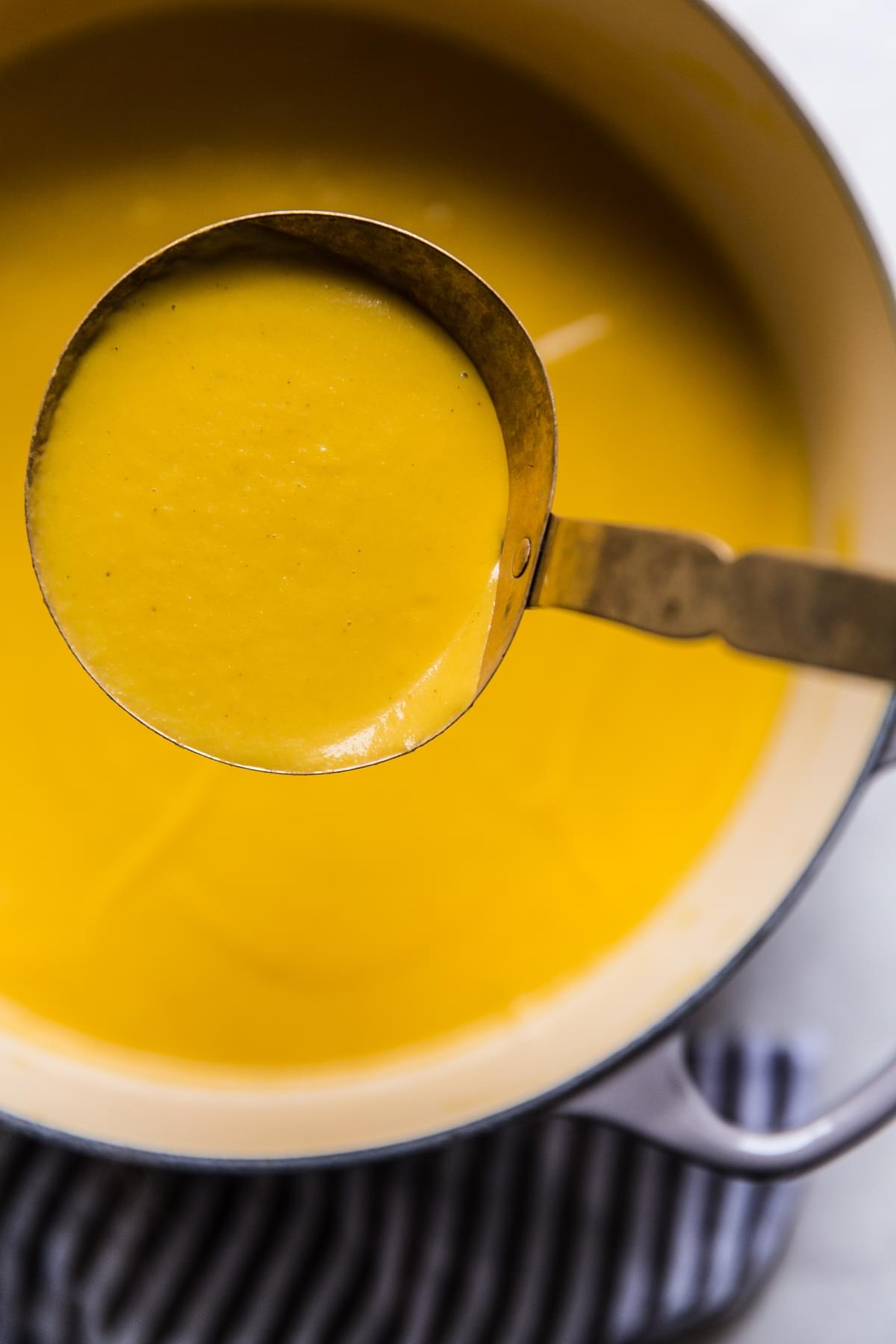 smooth and silky Roasted Butternut Squash Soup With Apples in a ladle over a soup pot