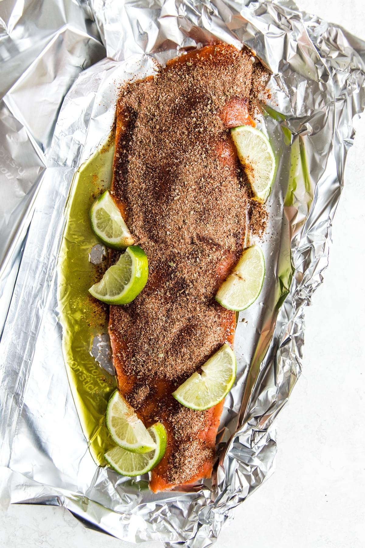 A fillet of salmon in foil with taco seasoning, limes and olive oil