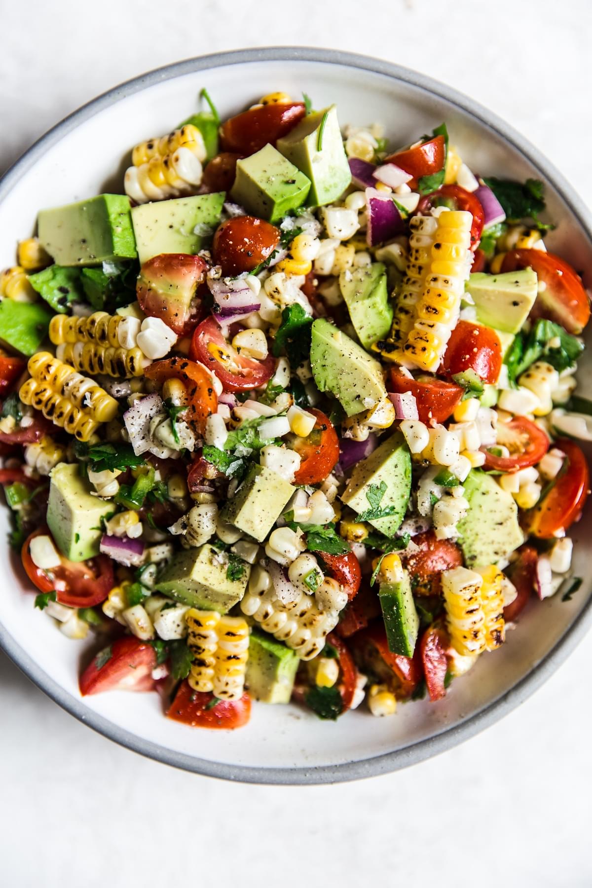 a corn and avocado salad in a bowl with tomatoes and cilantro
