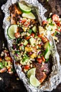 salmon in foil with avocado tomato salad in tin foil on a baking sheet