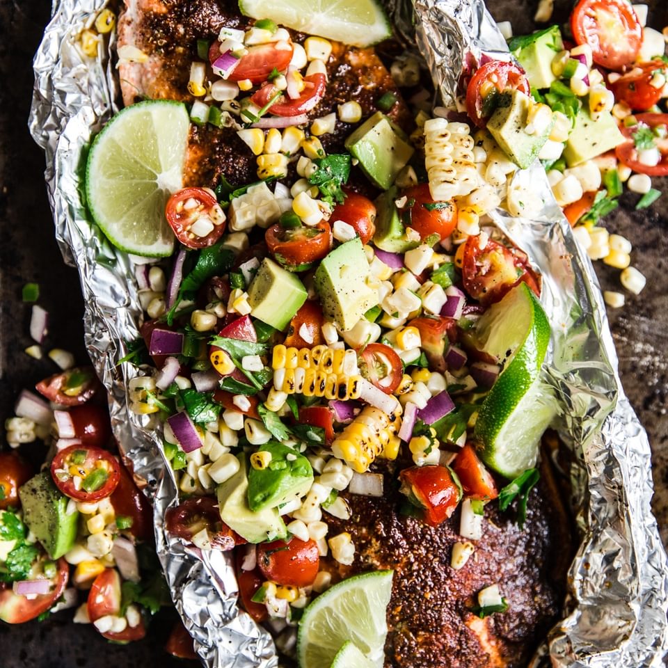 salmon in foil with avocado tomato salad in tin foil on a baking sheet
