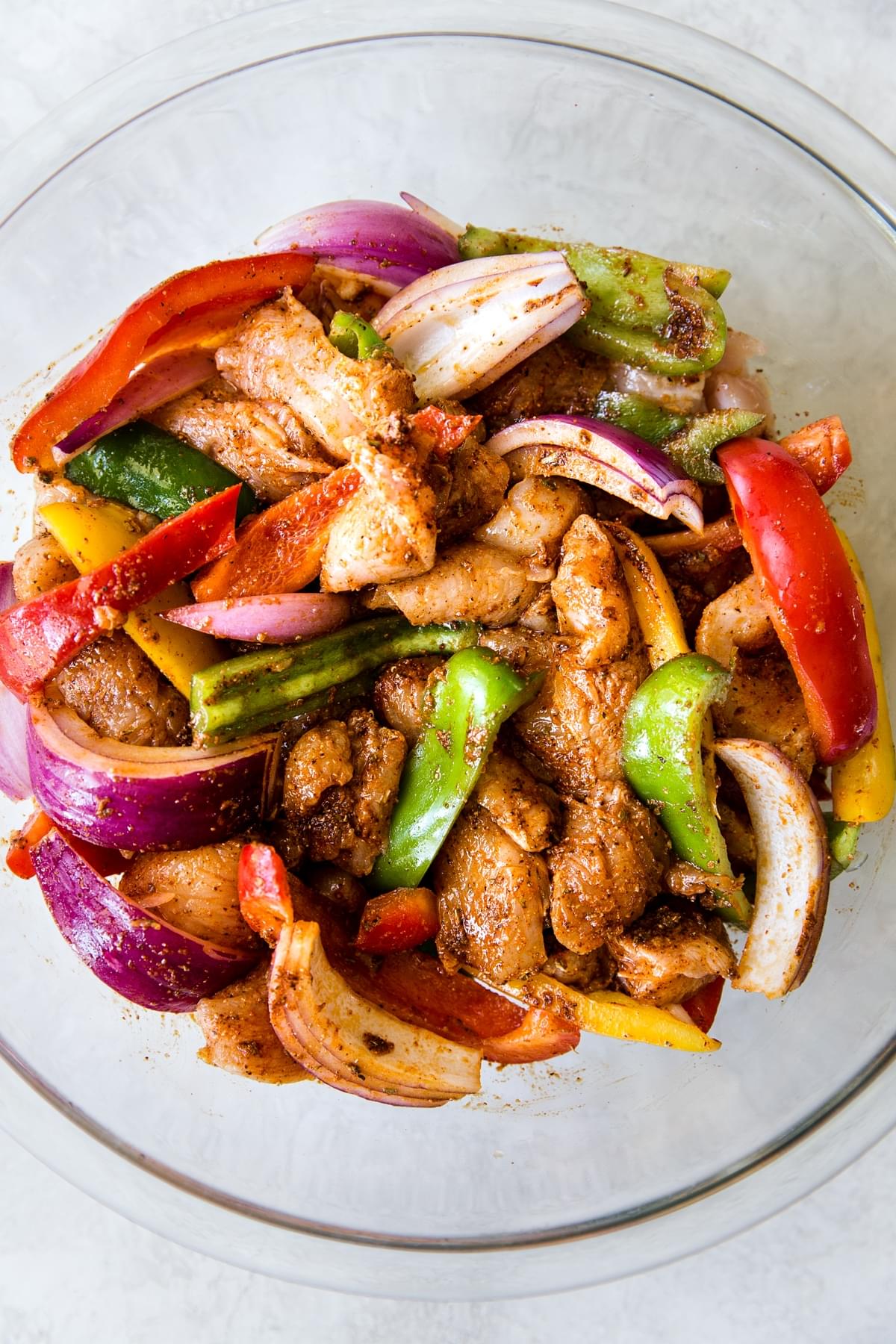 a glass bowl with chicken and bell peppers marinated in taco seasoning