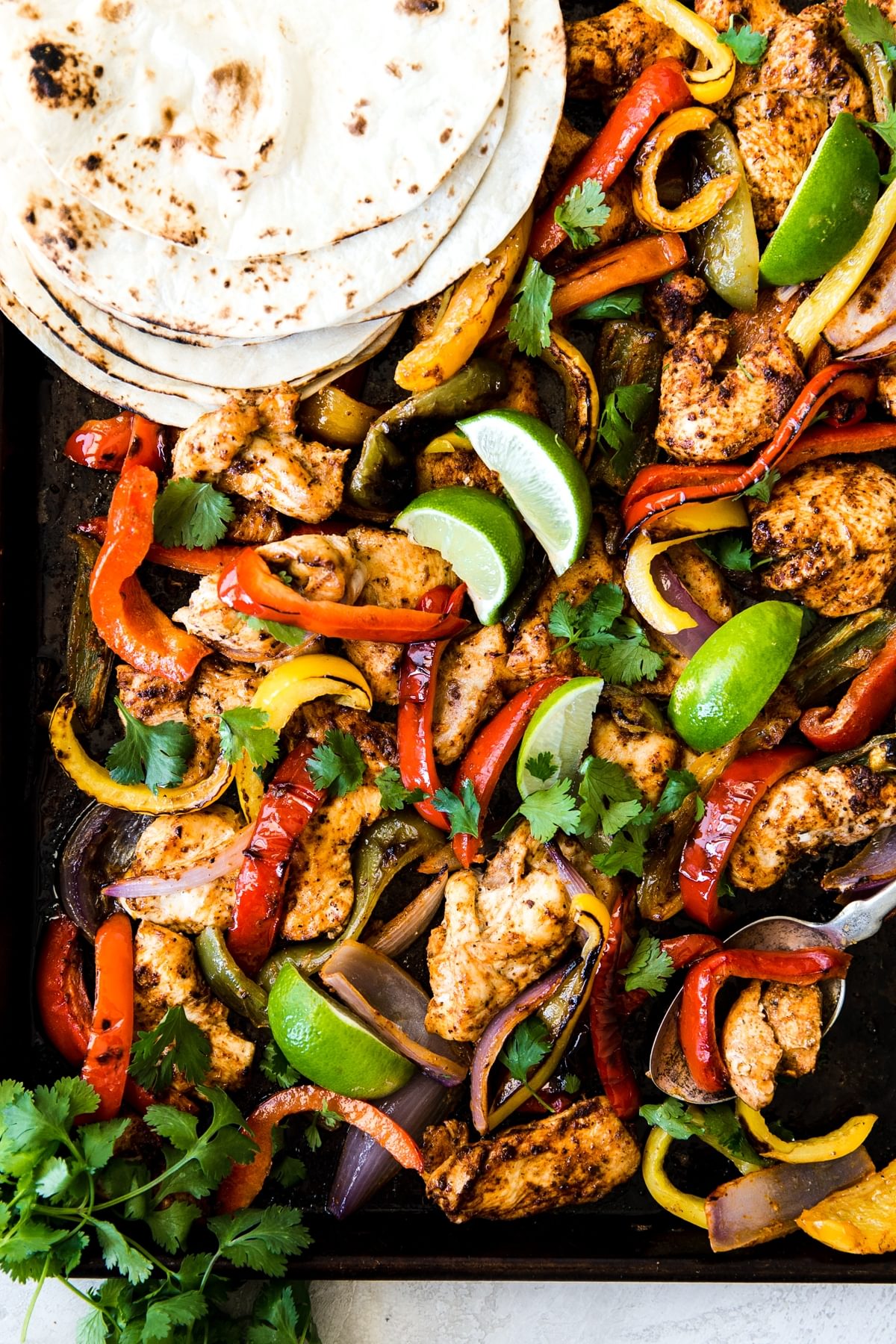 Chicken Fajitas on a sheet pan with onions, bell peppers, tortillas and a marinade.