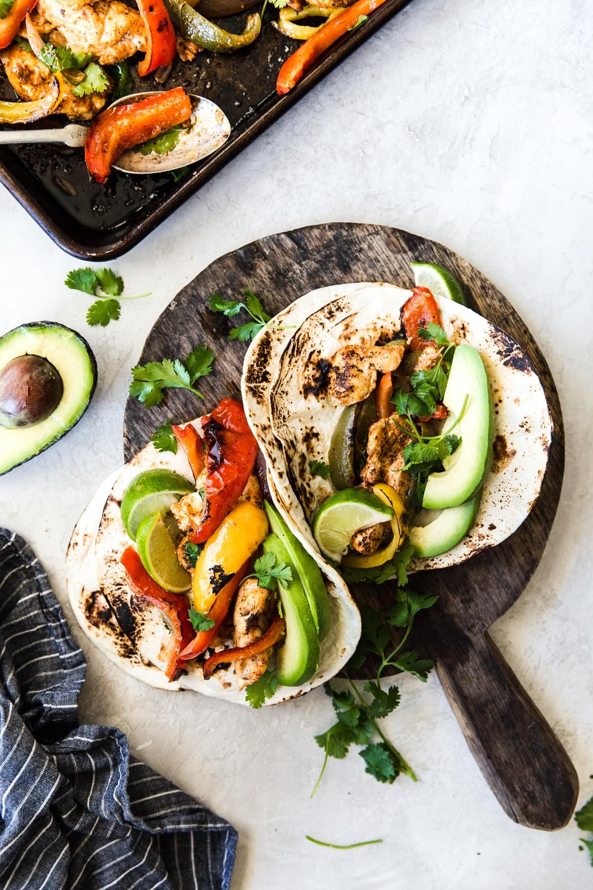 2 easy chicken fajitas on a plate with avocado, lime and bell peppers