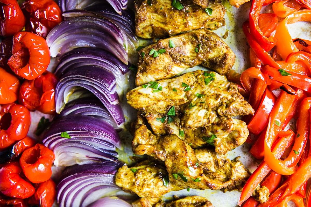 Sheet pan chicken shawarma with red bell peppers and red onion on a baking sheet