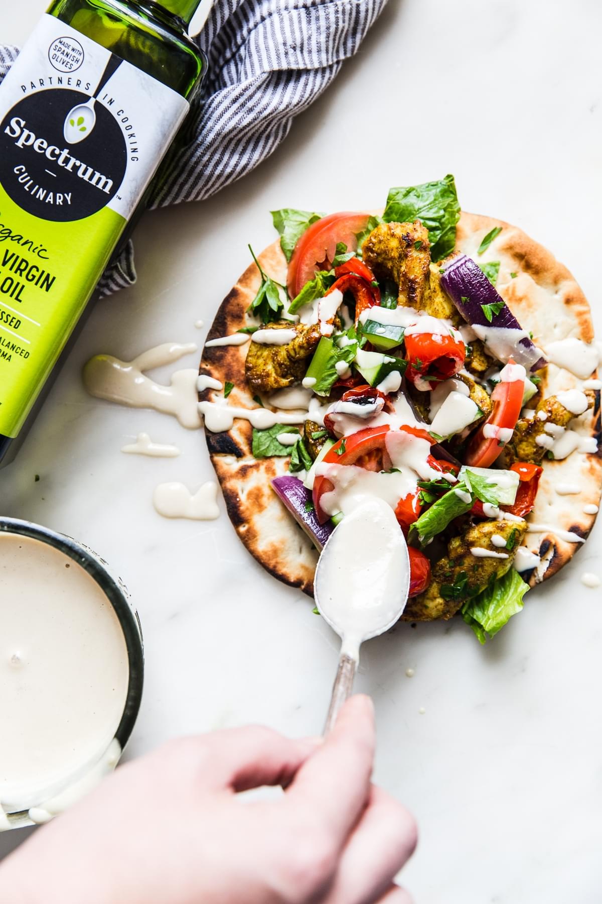 chicken shawarma on a pita being drizzled with tahini sauce
