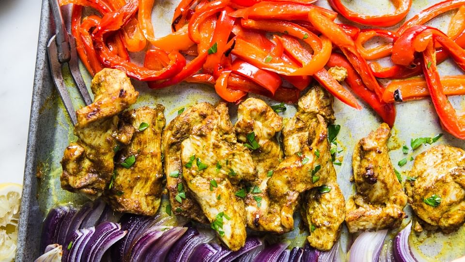 sheet pan chicken shawarma dinner with red onions and red bell peppers next to pita and parsley
