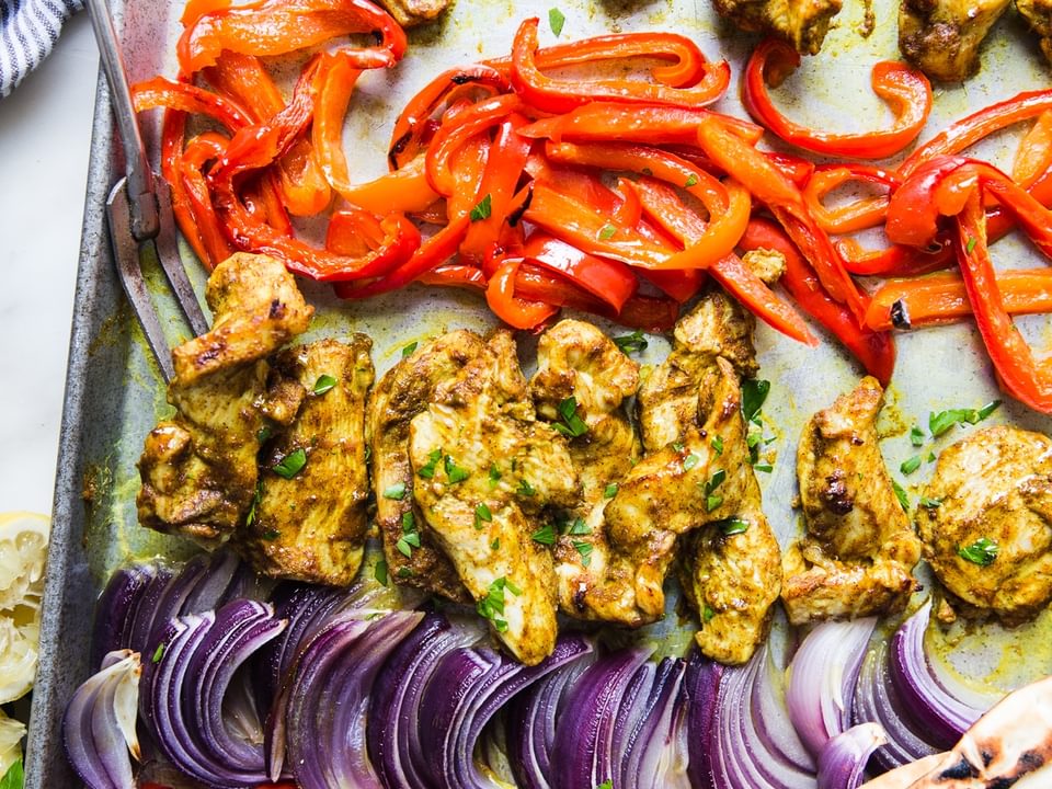 sheet pan chicken shawarma dinner with red onions and red bell peppers next to pita and parsley