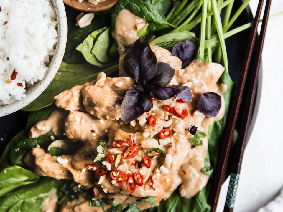 Slow Cooker Swimming Rama over spinach and peanuts on a plate with white rice and chop sticks